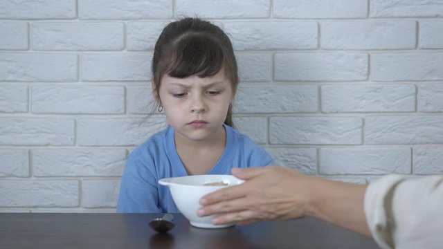 Oatmeal for breakfast. The mother gives her daughter oatmeal, the daughter refuses the porridge, pushing the plate away.