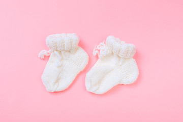 knitted baby booties on pastel pink background.