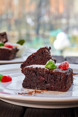 Slice of chocolate cake with candied fruit, mint and ice cream on a white plate and wooden background