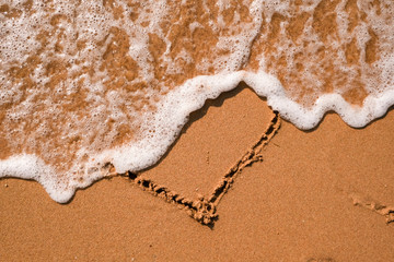 Heart drawn on sand, seacoast. Golden sand beach close up, summer holidays border frame concept.