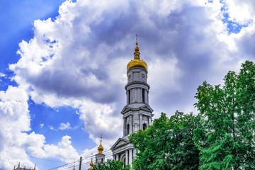 Fototapeta na wymiar Chapel with a golden dome of the Holy Dormition Cathedral in Kharkov against the background of a blue cloudy sky. Neoclassical bell tower of the Assumption temple on a sunny summer day