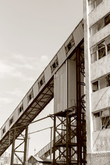 Old, abandoned concrete plant with iron rusty tanks and metal structures. The crisis, the fall of the economy, stop production capacity led to the collapse. Global catastrophe. Old photo effect