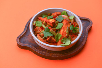 Stew of chicken meat with vegetables and pomegranate seeds served in a bowl over bright orange background.