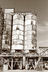 Old, abandoned concrete plant with iron rusty tanks and metal structures. The crisis, the fall of the economy, stop production capacity led to the collapse. Global catastrophe. Old photo effect