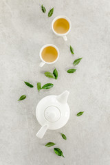 Fototapeta na wymiar Herbal tea with two white tea cups and teapot, with green tea leaves. Flat lay, top view. Tea concept