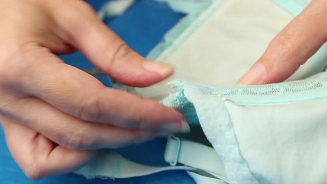 The woman inserts the iron bra bone that came out of the Cup of the blue bra. Close up.
