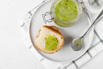 Green jam on the slice of bun on the ceramic plate. Top view. Served dessert