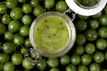 Gooseberry jam in a glass jar and berries scattered around. No-cook jam. Food background. Top view