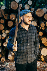 Portrait of a bearded brutal woodcutter holding hand saw