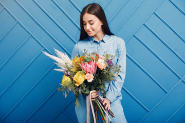Florist with flowers. Woman makes a bouquet. Girl on a blue background
