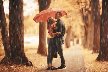 rain in the autumn park / young 25 years old couple man and woman walk under an umbrella in wet...