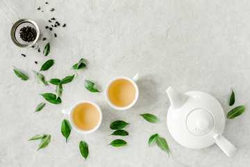 Obraz na płótnie Canvas Herbal tea with two white tea cups and teapot, with green tea leaves. Flat lay, top view. Tea concept