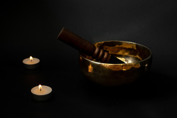 A Tibetan singing bowl on a black background surrounded by candles. Minimal design.