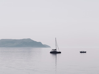 Minimal view of the sea, Crimea. Morning seascape with a lonely boat floating in the middle of the sea and overlooking the mountains in the haze. Minimalism. - 371149621