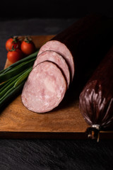 Food composition with sliced dry smoked sausage on a cutting board, focus on slices.