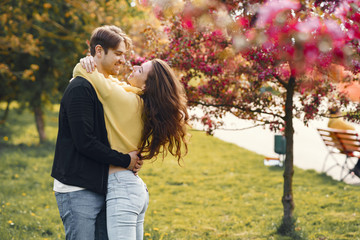 Fototapeta premium Cute couple in a park. Man in a black jacket. People walks. Couple near blooming trees