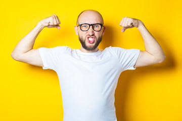 Fototapeta premium Bald young man with a beard shows muscles, strength on a yellow background.