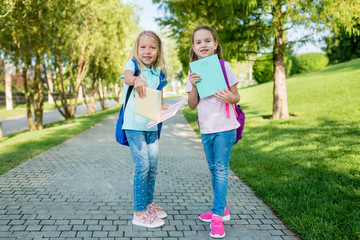 First day at school. Two cute pupils girls with backpack and books going to lessons in sunny day.  School Days with friends. Concept back to school