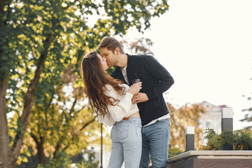 Cute couple in a city. Man in a black jacket. People walks. Girl drinks a coffee.