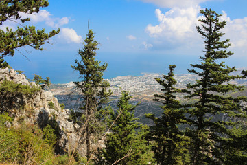 Obraz premium View from above between the fir trees and the stone wall of the castle of Saint Hilarion on the city of Kyrenia and the Mediterranean sea. Cyprus...