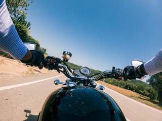 Driving an old black motorcycle driver point of view on a summer landscape solid blue sky