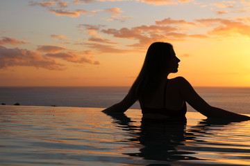Silhouette of a girl with long loose hair,who stands at the edge of the pool and looks at the...