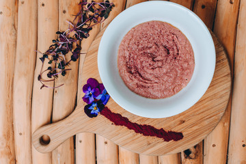 Strawberry Keto porridge on a wooden serving board with some purple powder, flowers and leaves