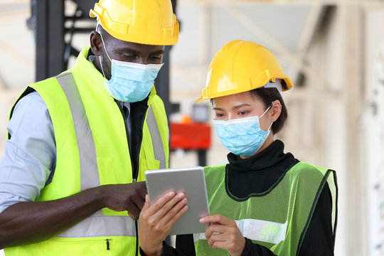 African American and Asian workers wearing facial mask and safety vest working in warehouse checking for the inventory using digital tablet during new normal after covid-19