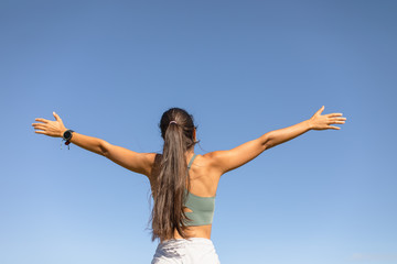 Healthy fitness lifestyle success. Back view of sporty blissful fit young woman raising arms to the sky.