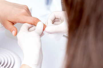 Manicure master removing nail polish with white cotton pad in beauty salon