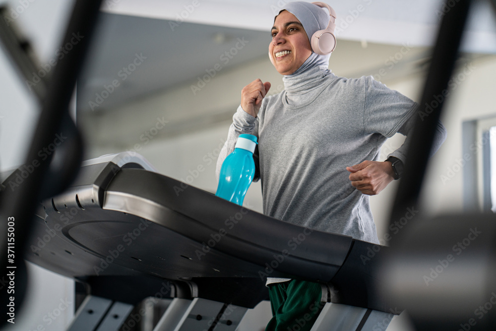 Wall mural muslim adult woman with headphones on treadmill