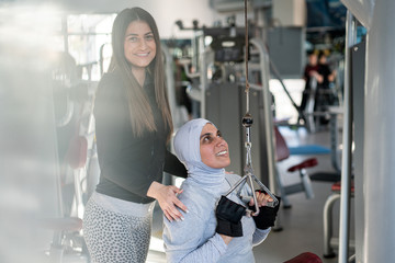 Fototapeta premium Fitness trainer assisting a muslim woman in gym
