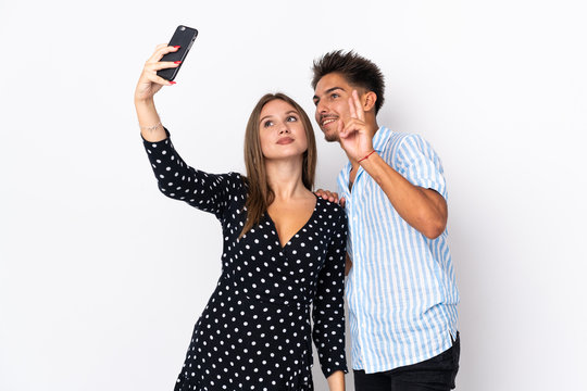 Young caucasian couple isolated on white background making a selfie with the mobile