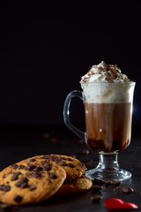 Close up of a glass cup of coffee with whipped cream and chocolate on it, chocolate chip cookies...