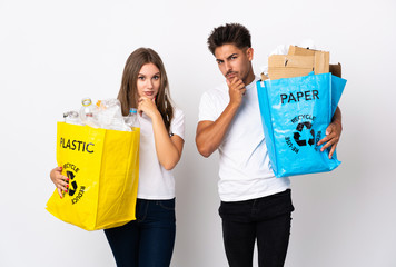 Young couple holding a bag full of plastic and paper isolated on white background thinking