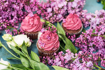 Three purple cupcakes with roses and lilac on blue table