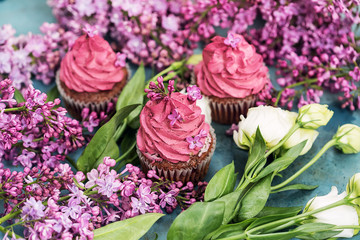 Three purple cupcakes with white roses and lilac on blue table