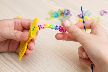 Rubber Band Weaving. Knitting rubber bands with loom knit. Hands of girl weaving wristband of rubber bands.