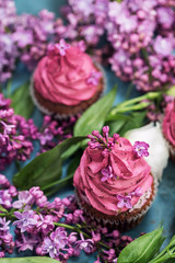 Two pink cupcakes among purple lilac and white rose
