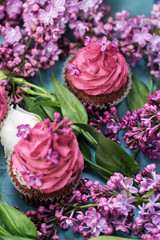 Two pink cupcakes among purple lilac on blue table