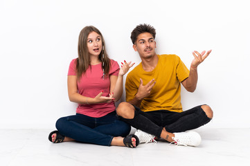 Fototapeta na wymiar Young couple sitting on the floor isolated on white background extending hands to the side for inviting to come