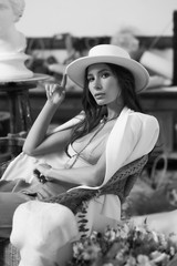 Beautiful pretty elegant woman sitting in armchair in art studio or class between sculptures. Stylish female wearing green top, palazzo trousers, white hat and blazer. Fashion indoor portrait