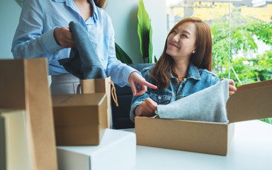 Two young women receiving and opening a postal parcel box of clothing at home for delivery and online shopping concept