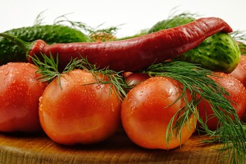 Green dill, cucumbers, chili peppers and tomatoes lie on a wooden board