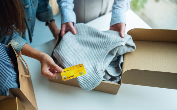 Closeup image of women holding and using credit card for online shopping while opening a postal parcel box of clothing at home