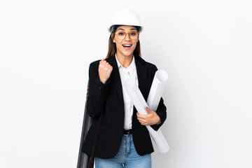 Young architect caucasian woman with helmet and holding blueprints over isolated background celebrating a victory