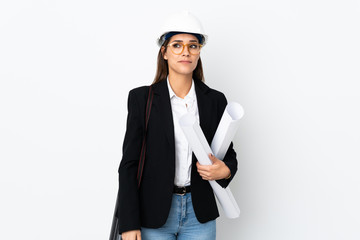 Young architect caucasian woman with helmet and holding blueprints over isolated background standing and looking to the side