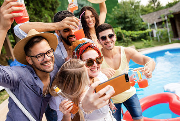 Obraz premium Group of young people having fun at summer vacation and enjoying a poolside party with drinks and making selfie.