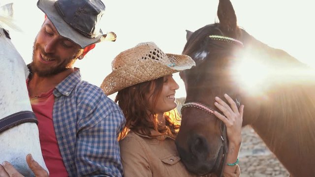 Animals lovers couple taking with bitless horses during sunny day inside ranch corral - Happy people having fun training at their farm - Love and wild concept 