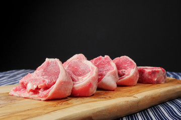 Stack of fresh raw lamb loin chops on a wooden board and white and blue table cloth, black background. Meat industry concept.
